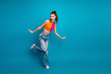 Charming young woman posing playfully in vibrant outfit against a blue background, expressing...