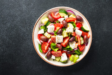 Greek salad in craft plate on black kitchen table. Top view. Vegan food.