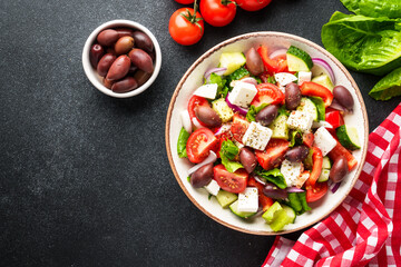 Greek salad in craft plate on black kitchen table. Top view. Vegan food.