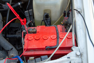 A close-up view of a car's engine compartment featuring a bright red battery with connected cables...