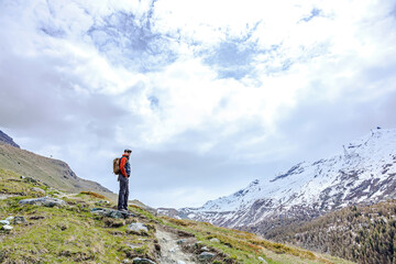A hiker with a backpack stands on a trail, admiring a breathtaking mountain view