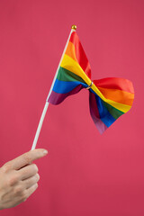Woman holding rainbow flag fastened with wedding ring on pink background. 