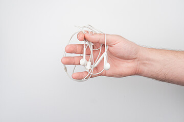 A hand holding a pair of tangled earbuds sits on a light-colored, nondescript surface under even...