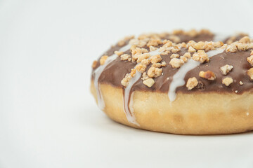 Close-up shot of a dark chocolate peanut doughnut on a light gray surface, with contrasting texture and detail due to shallow depth of field and bright lighting