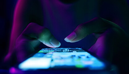 Finger of woman touching scroll page app on mobile phone.In a room with blue and purple neon...