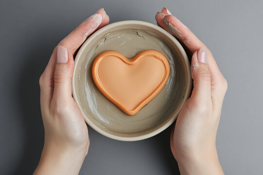 Hands crafting a heart-shaped design in clay during pottery session in a workshop