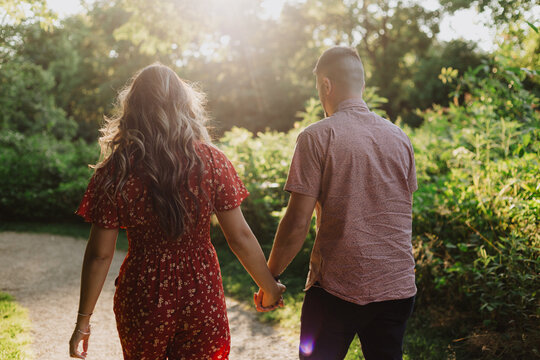 Couple holding hands walking on sunlit forest path