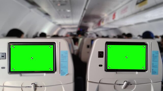 Interior view of a commercial airplane cabin with rows of passenger seats and seatback entertainment screens showing green screen placeholders, suitable for mockups or chroma key replacements