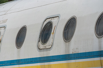 Close-up of a white passenger airplane with reflective, evenly spaced round windows and yellow...