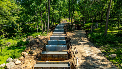 A new trail is being constructed in a green forested area. Wooden planks line part of the path, while concrete forms are laid out in an organized manner. Heavy machinery is present in the background. © Greg Kelton