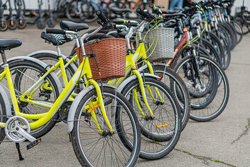 Two parallel rows of yellow bicycles with black wheels and wicker baskets, parked outdoors Diagonal arrangement from left to right, with a partially visible third row in the background No branding