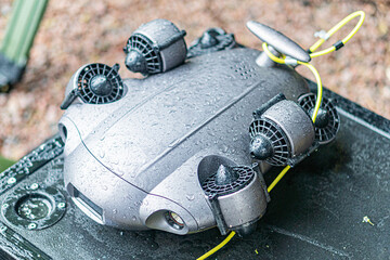 Close-up image of a gray and black drone with yellow cables, resting outdoors on a flat surface
