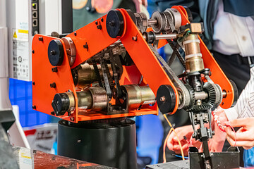 Image of a robot arm with an orange exterior and intricate mechanical components on a blue-tiled...