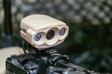 Robotic demining arm, outdoor setting suggested by greenery, tan-colored mechanical structure,...