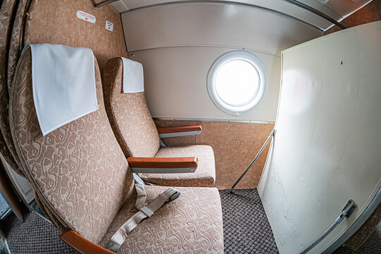 Small, compact airplane cockpit with controls and instruments Beige upholstery and white patterned seat covers Bright, daytime lighting Empty cockpit interior Candid photograph of a passenger air