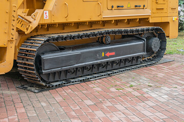 Close-up of an excavator, primarily metallic in color, partially visible on a brick surface under...