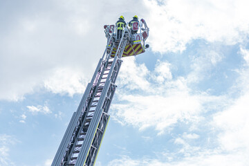 Emergency vehicle with extendable ladder, outdoor setting, clear daylight, three individuals in safety gear on the ladder, possible maintenance or rescue operations