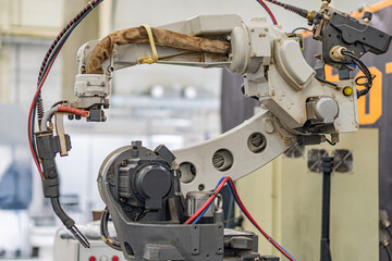 Side view of an industrial robot with articulated joints, connected to a control panel and cables,...