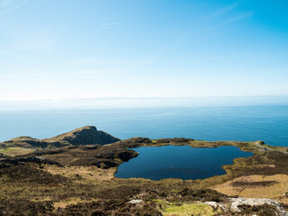 Blue sky reflects in puddle of water, ocean in the background, scene at stunning Slieve League cliffs in county Donegal, Ireland. Popular tourist area for sightseeing and hiking.