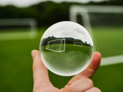 Football or soccer goal posts in glass ball which is hold by a someone hand. Forecasting sport results in popular world sport. Betting on club and national teams concept. Selective focus.