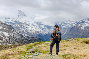 A hiker stands on a trail in the Swiss Alps, gazing at the breathtaking mountains.