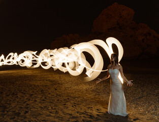Long exposure photograph of a beautiful girl in a wedding dress posing elegantly at night on the...