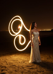 Long exposure photograph of an attractive Caucasian girl in an evening gown posing on the beach at...