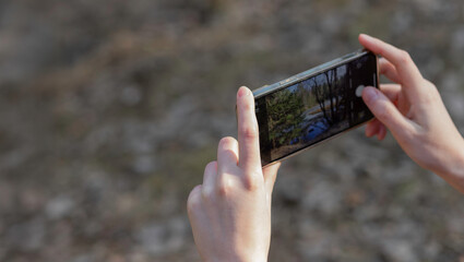 holding a smartphone to take a photo, capturing a shot of nature. Modern mobile device used for