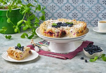 Shortcrust pie with custard filling and fresh honeysuckle or blueberries on a cake stand on a grey...