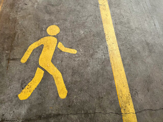 Yellow walking figure approaching yellow dividing line painted on a gray concrete floor