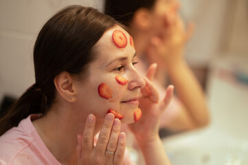 girl's face in front of the mirror, a woman applies a mask of natural strawberries. Applying fresh...