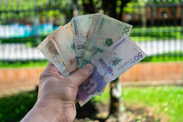 Colombian peso bills held by a man, blurred background outdoors