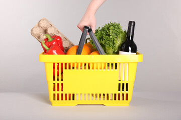 Woman with shopping basket full of products on gray background, closeup