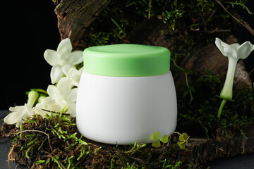 Jar of moisturizing body cream on tree bark with plants and flowers, closeup