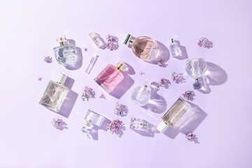 Luxury perfumes and beautiful lilac flowers on light violet background, flat lay