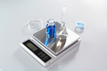 Scale with samples and laboratory glassware on white table in color lights, closeup
