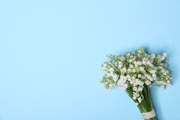 Beautiful lily-of-the-valley flowers on light blue background, top view. Space for text