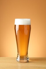 Fresh beer in glass on wooden table against beige gradient background, closeup