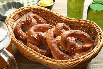 Tasty pretzels in basket and beer on wooden table, closeup