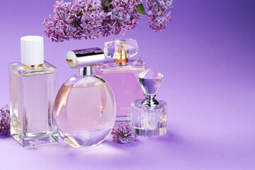 Bottles with perfumes and lilac flowers on purple gradient background, closeup. Space for text