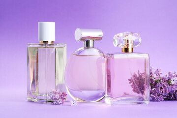 Bottles with perfumes and lilac flowers on purple gradient background, closeup