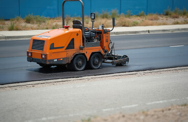 Asphalt concrete road cutting machine working beside curb. Orange machinery cuts pavement, repairing road. Road construction industry, asphalt cutter, road work in progress. Heavy machine performs