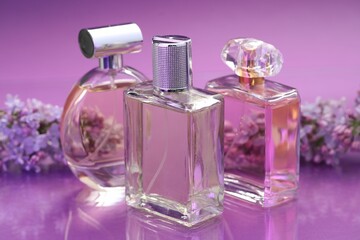 Bottles with perfumes and lilac flowers on mirror surface against color gradient background, closeup