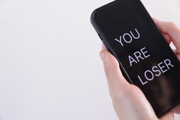 Cyber bullying. Woman holding smartphone with text You Are Loser on white background, closeup. Space for text