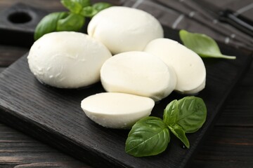 Pieces of delicious mozzarella cheese and basil in bowl on wooden table, closeup