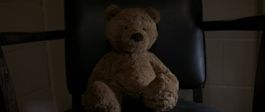 Teddy bear sits alone in dark room
