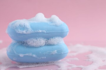 Soap bars with foam on pink background, closeup. Space for text