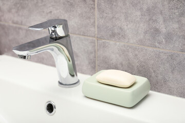 Soap bar near faucet on sink in bathroom, closeup