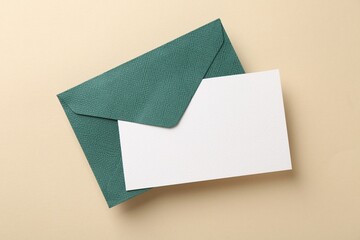 Blank invitation card and envelope on beige background, top view