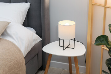 Side table with lamp near bed indoors
